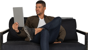 Front view of a bored young man sitting on a sofa while watching the tablet