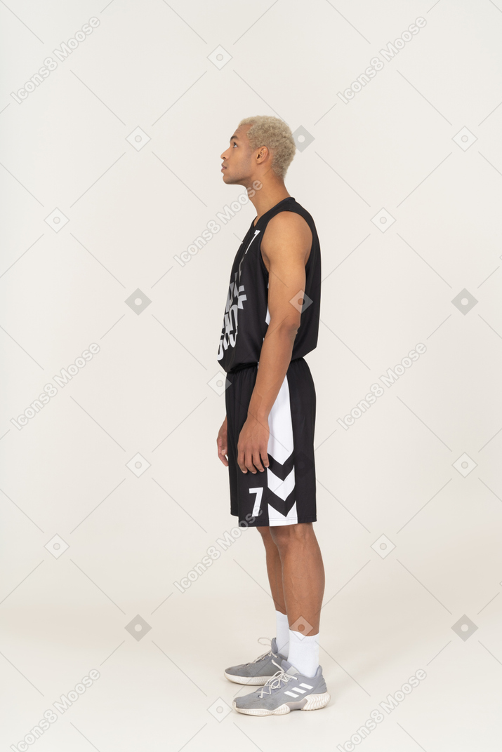 Vista laterale di un giovane giocatore di basket maschile in piedi immobile e guardando in alto