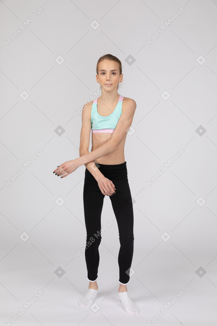 一个年轻的女孩，在运动服穿越手中，同时看着相机的前视图