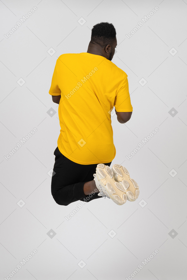 Vista posterior de un joven de piel oscura saltando en camiseta amarilla