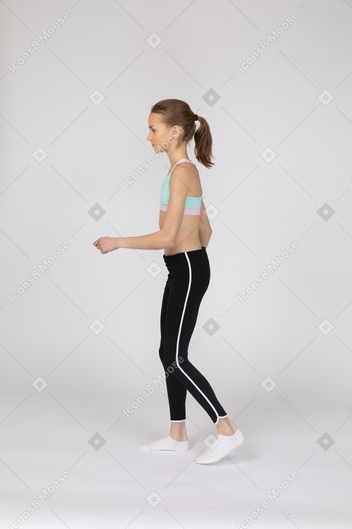 Side view of a teen girl in sportswear walking and raising hand