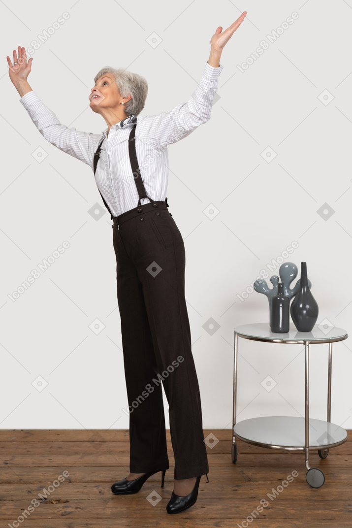 Three-quarter view of an old lady in office clothing raising hands while looking for something