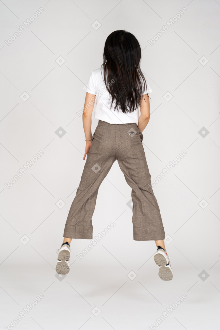 Back view of a jumping young lady in breeches and t-shirt outspreading her legs