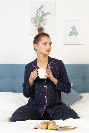 Vue de face d'une jeune femme en pyjama prenant son petit déjeuner au lit