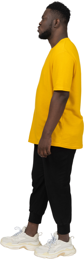 Vista lateral de um jovem de pele escura fazendo beicinho em uma camiseta amarela parado