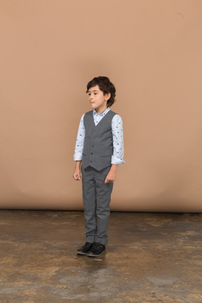 一个穿着灰色西装的可爱男孩站着不动，望向一边的前视图