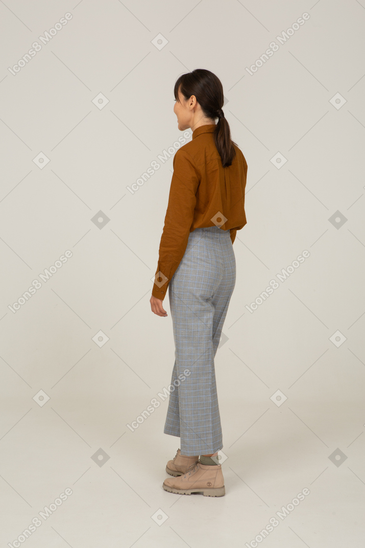 一位身着马裤和衬衫的年轻亚洲女性站在四分之三的后视图