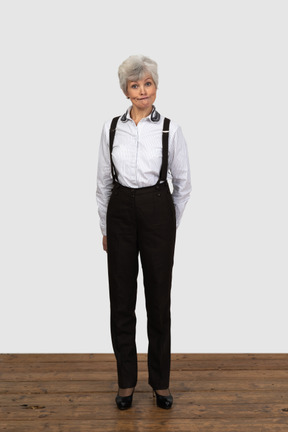 Vista frontal de una anciana perpleja en ropa de oficina haciendo muecas con las manos detrás de la espalda