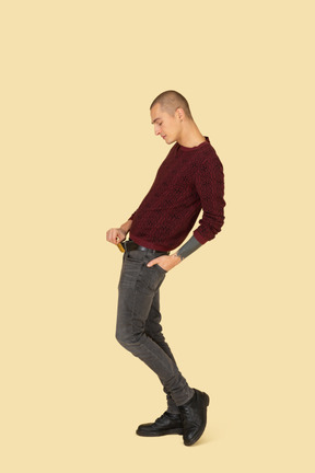 Side view of a young man in red pullover touching belt while leaning back