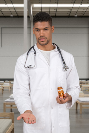 A male doctor holding a pill and a pill bottle in his hands
