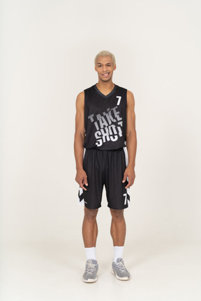 Vista frontale di un giovane giocatore di basket maschio sorridente che fa l'occhiolino in piedi immobile