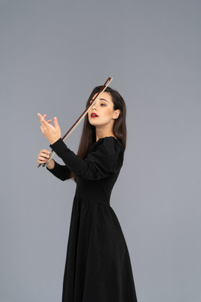 Vue de trois quarts d'une jeune femme en robe noire faisant l'impression de jouer du violon