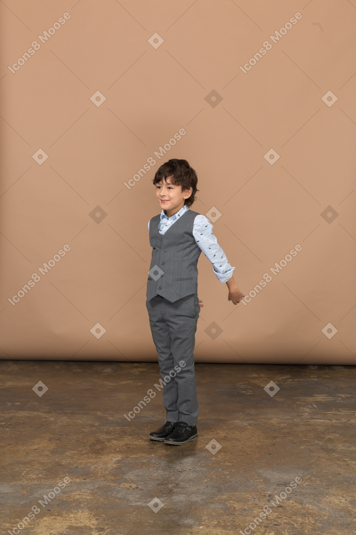 Front view of a boy in suit standing with outstrerched arm
