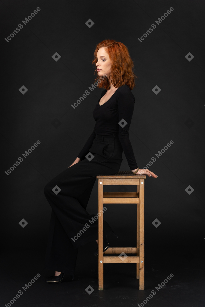 A side view of the beautiful young woman dressed in black and sitting on the wooden chair with closed eyes