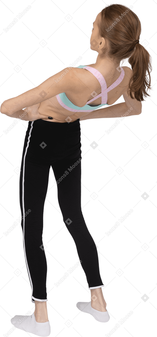 Vista posteriore di tre quarti di una ragazza adolescente in abbigliamento sportivo che mette le mani sui fianchi mentre si appoggia indietro