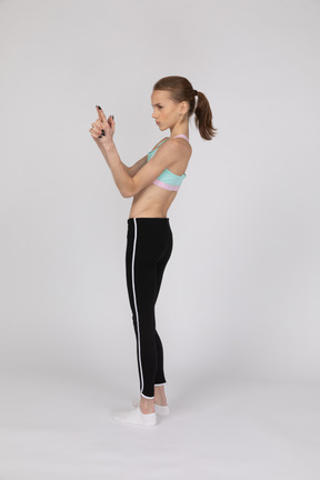 Vista lateral de uma adolescente em roupas esportivas fazendo gesto de arma de dedo