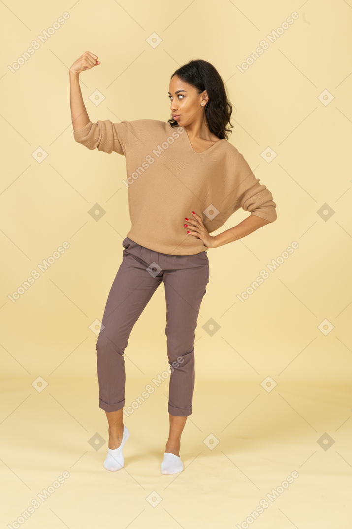 Vista frontal de una mujer joven de piel oscura fuerte levantando la mano mientras pone la mano en la cadera