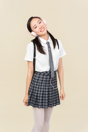 Asian school girl adjusting headphones and looking up
