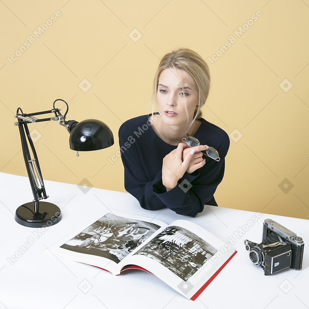 Jovem mulher sentada à mesa e segurando seus óculos