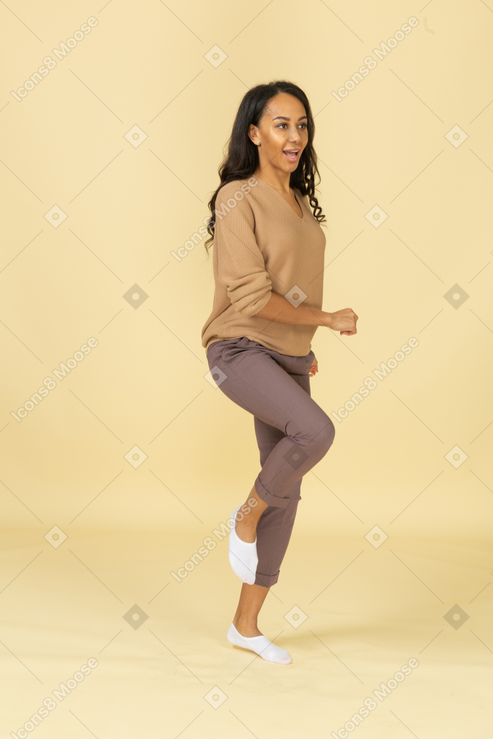 Three-quarter view of a marching dark-skinned young female raising leg