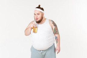 A fat man in sportswear drinking beer from the bottle