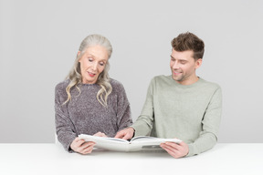 Elegant old woman and young guy going through a book together