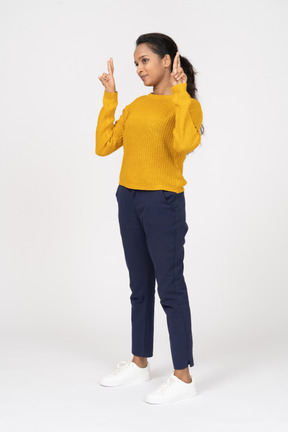 Vista lateral de uma garota com roupas casuais apontando para cima com os dedos