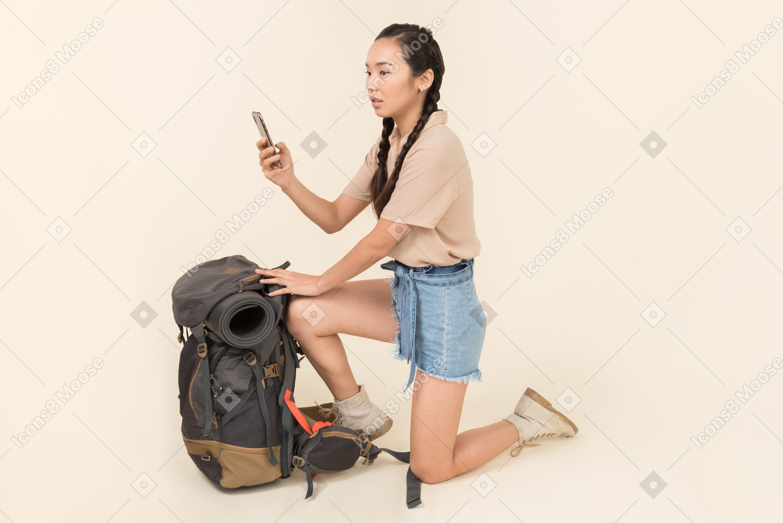 Оскорбленная молодая азиатская женщина, стоящая возле рюкзака и делающая снимок со смартфона