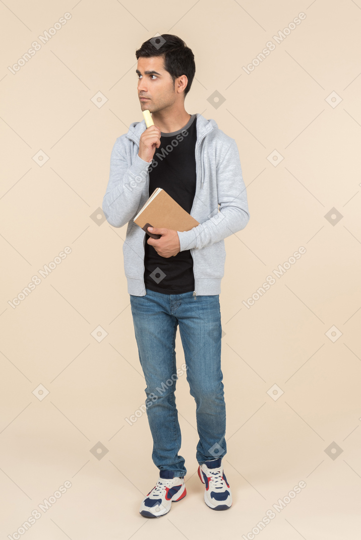 Young caucasian man thinking while holding a notebook and a pen