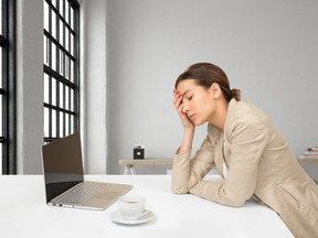 Une femme assise à la table du bureau a posé la main sur le front et a fermé les yeux.