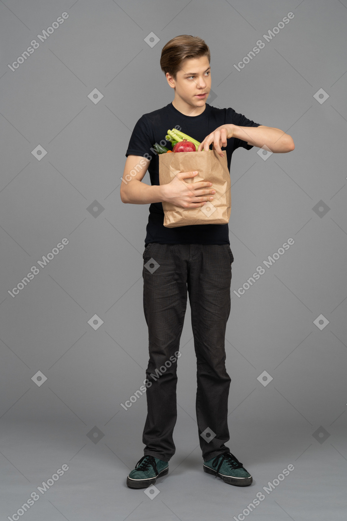 Jovem olhando de soslaio enquanto pega um vegetal de um saco de papel