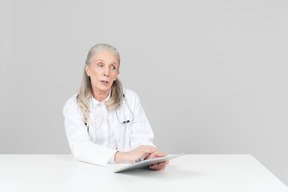 Âgée femme médecin travaillant sur une tablette numérique