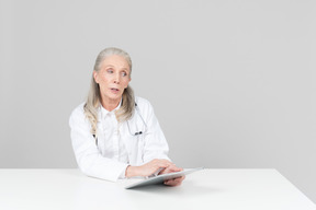 Aged female doctor working on a digital tablet