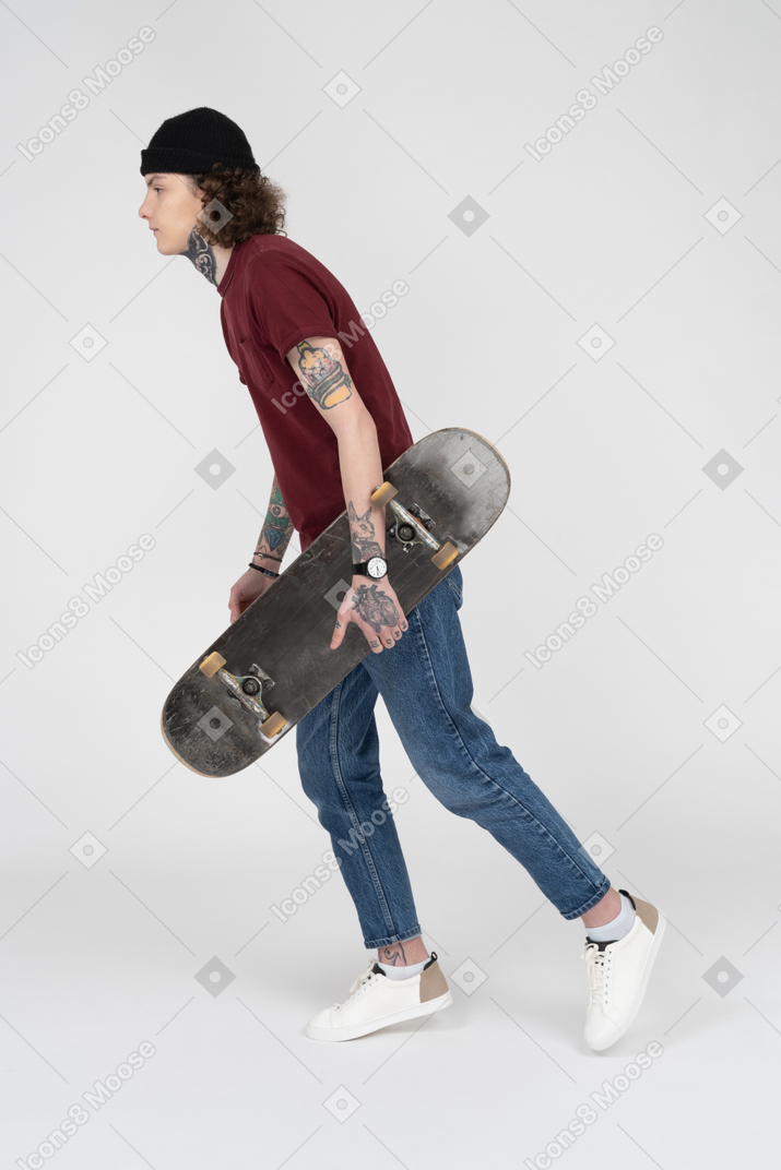 彼のスケートボードを持って歩くティーンエイジャー