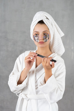 Mujer en bata de baño limandose las uñas