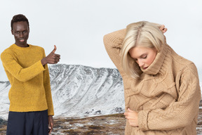 Mujer con suéter cálido y hombre mostrando los pulgares hacia arriba