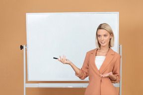 Jolie femme debout à côté d'un tableau blanc et expliquer quelque chose