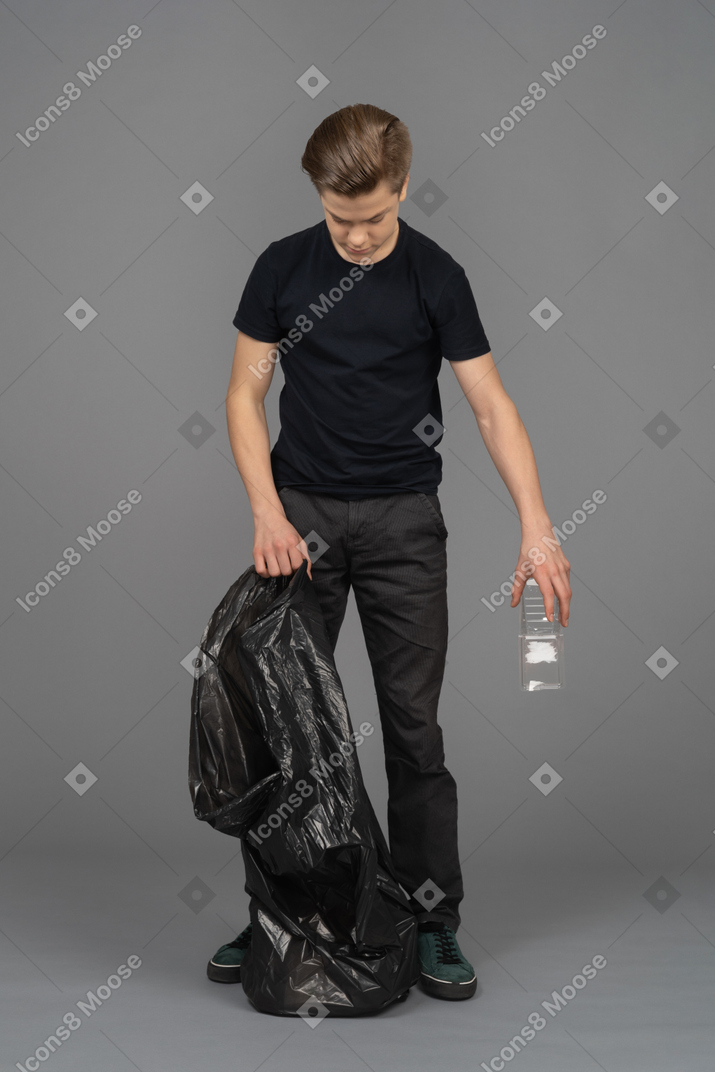 Un giovane in possesso di un sacco della spazzatura e una bottiglia di plastica