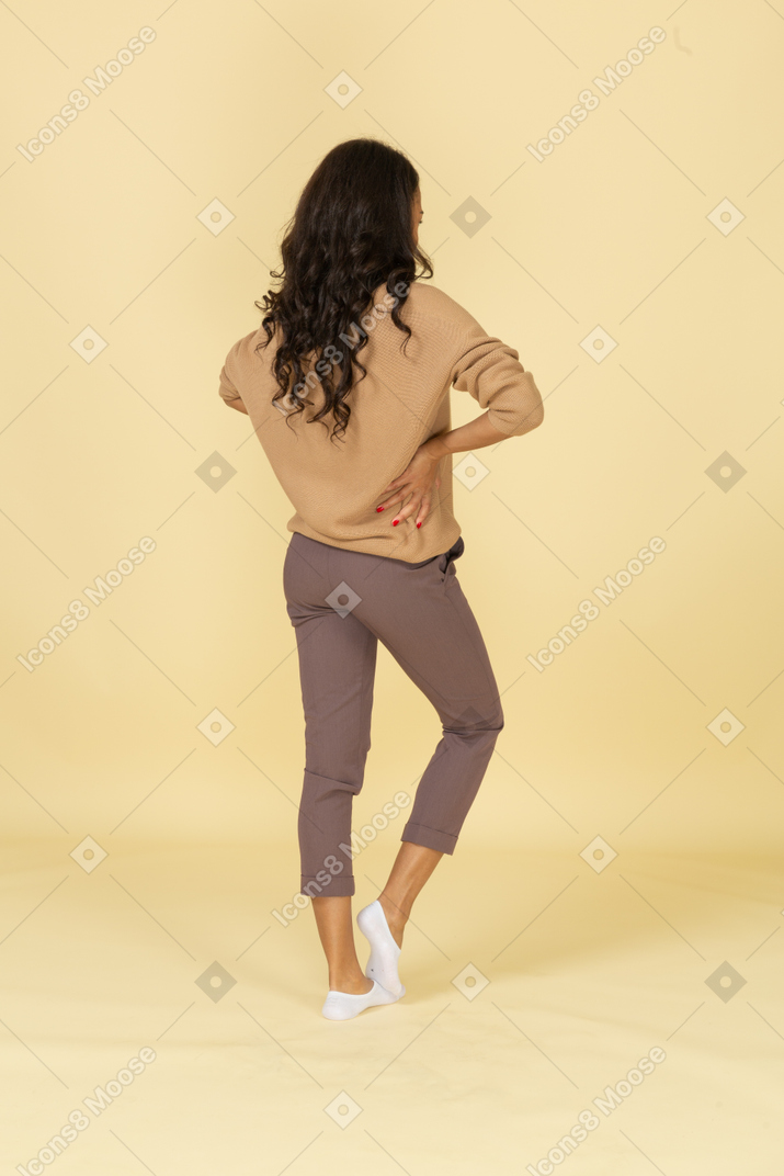 Vista posteriore di tre quarti di una giovane femmina allegra dalla carnagione scura che mette le mani sui fianchi