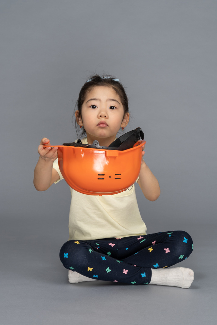 Front view of a little girl holding an orange hard hat