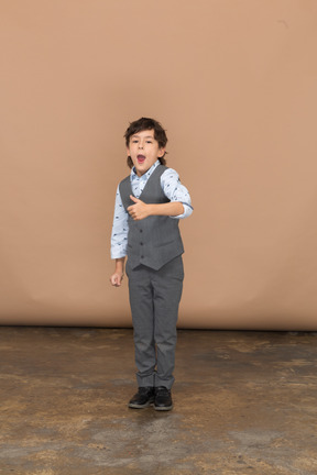 Vista frontal de un chico lindo con traje gris que muestra el pulgar hacia arriba