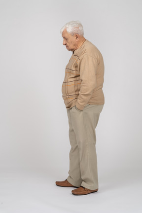 Side view of an old man in casual clothes standing with hands in pockets