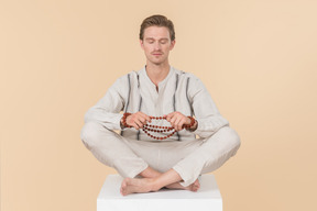 Young caucasian man sitting in lotus position holding necklace