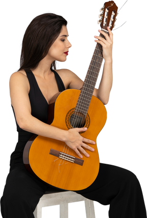 Vista frontal de uma jovem sentada de terno preto olhando para o violão