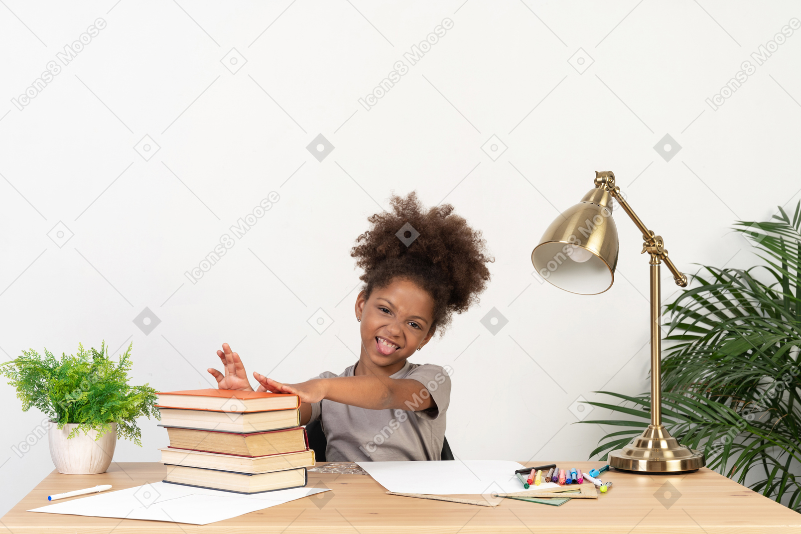 Prudent girl sitting at a table with books and showing her tongue