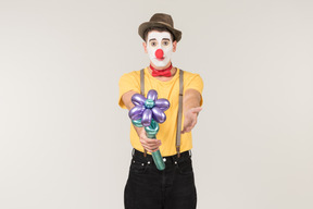 Male clown pointing at flower he's holding