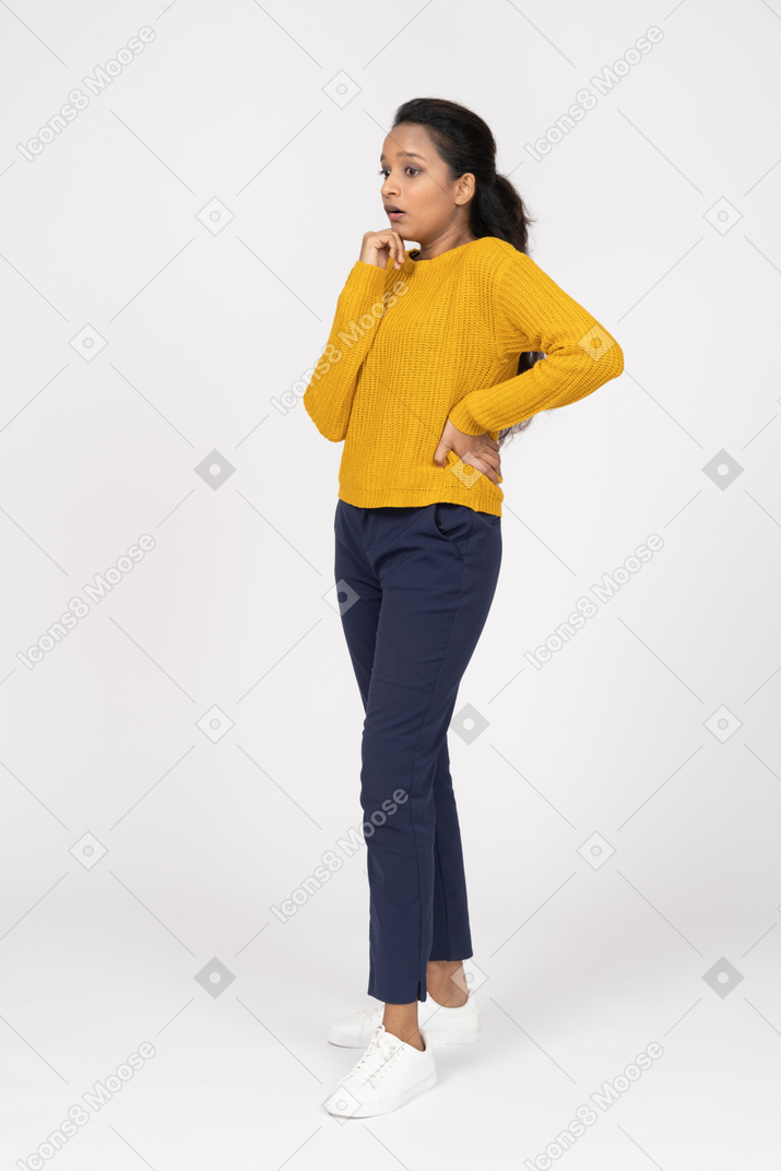 Vista lateral de uma garota pensativa em roupas casuais, posando com a mão no quadril