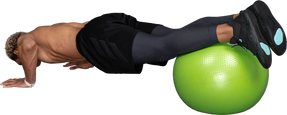 Three-quarter back view of a shirtless afro man making push-ups on a gym ball
