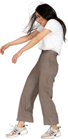Vista laterale di una giovane donna in calzoni e t-shirt tese le mani