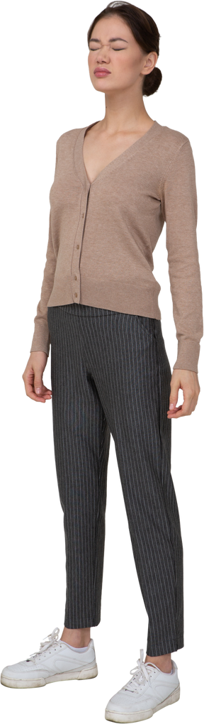 Vista de tres cuartos de una joven en suéter y pantalones de pie con los ojos cerrados